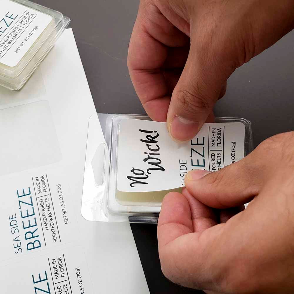Person applying 3" x 2" white matte wax melt container label