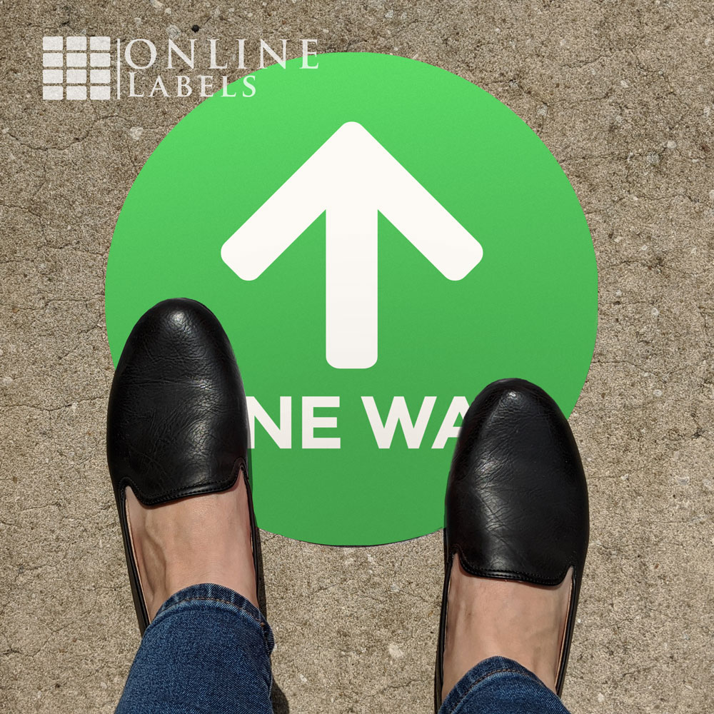 Feet near green "one way" wayfinding floor sign for covid safety