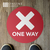 Feet on red "one way" floor sign for guiding customers through aisles during covid; wrong way sticker