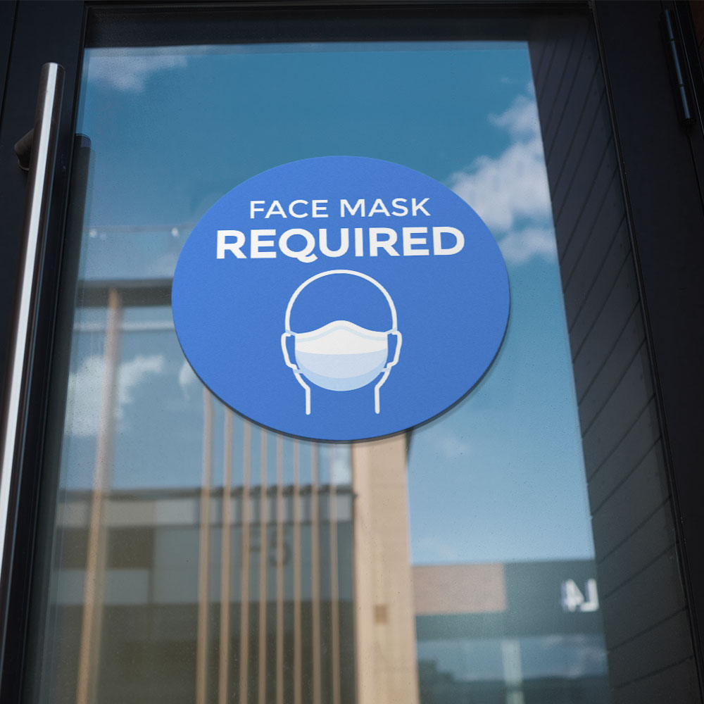 Blue "face mask required" window/wall sticker on glass door pane of office building downtown