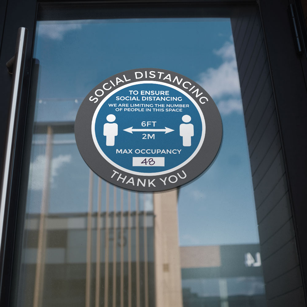 Blue "Social distancing, to ensure social distancing, we are limiting the number of people in this space, max occupancy: __, 6 FT, 2M, thank you" window/wall sticker on glass door pane of office building downtown